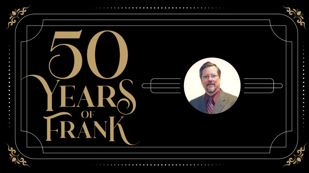 The image is a graphic design celebrating "50 Years of Frank." The design has a black background with elegant gold lettering on the left side that reads "50 Years of Frank" in a stylized font. On the right side of the image, there is a circular photo of a man with short hair, a beard, and glasses, wearing a suit and tie. The photo is bordered by thin gold lines that extend horizontally across the graphic, adding to the sophisticated and celebratory feel of the design. The corners of the image are adorned with small, ornate gold details, enhancing the overall formal and elegant theme.