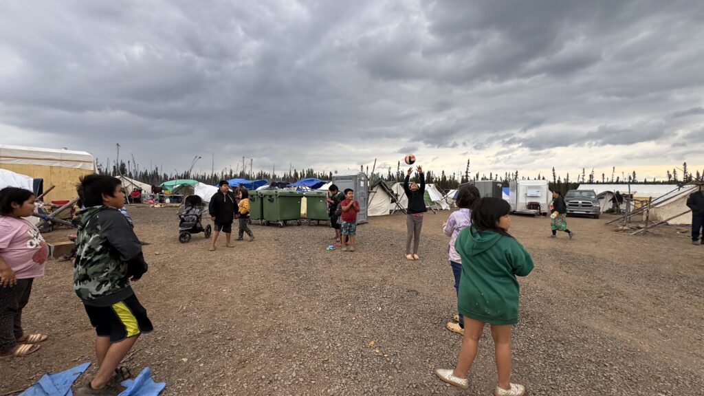 Another shot of the children’s volleyball game, showing the ball in play as it moves between the kids. Tents and portable restrooms are visible in the background, and the sky remains dark with storm clouds, though the children are undeterred.