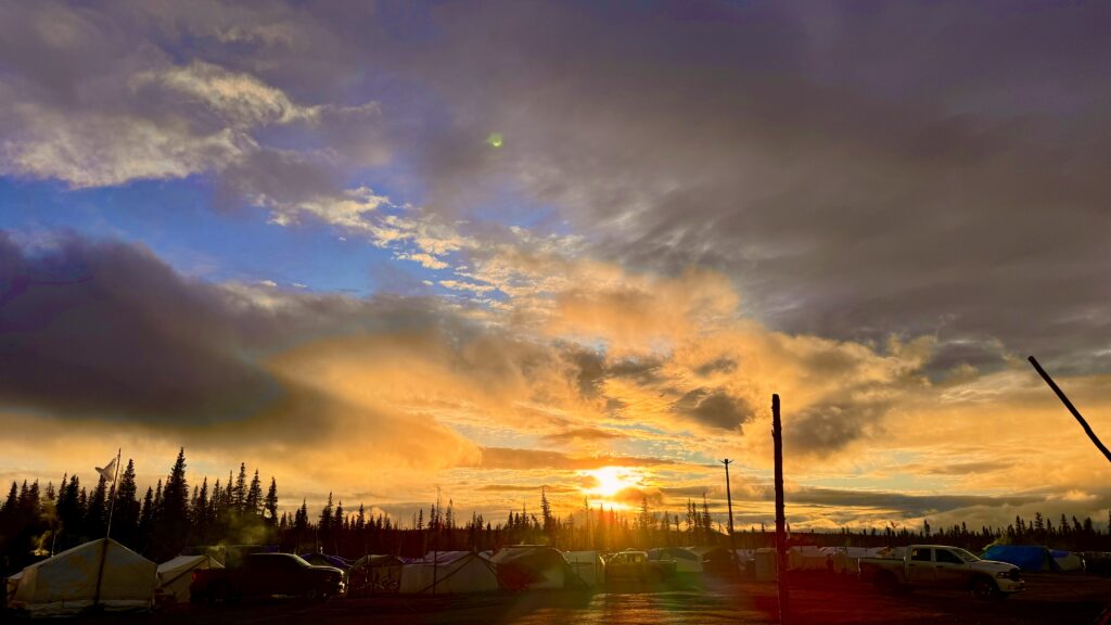 The golden hues from the setting sun created a breathtaking scene at the camp as the last remnants of the storm drifted away, leaving behind a sky filled with clouds illuminated in soft oranges and purples.