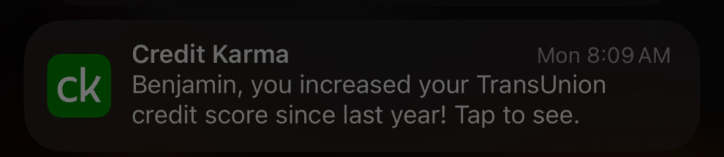 This image shows a smartphone notification from the Credit Karma app. The message reads: "Benjamin, you increased your TransUnion credit score since last year! Tap to see." The notification includes the Credit Karma logo and was received at 8:09 AM on a Monday. The contrast between being in a remote location and receiving a credit score update adds a sense of irony to the moment.