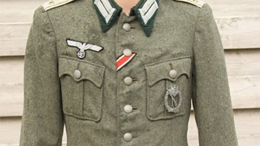 The image shows a military uniform jacket from World War II, featuring Nazi insignia, including the eagle and swastika emblem on the chest and various other patches and decorations. The style and symbols indicate it is a German Wehrmacht or similar uniform.