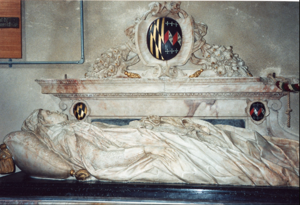 A marble tomb effigy of a figure lying in repose, draped in detailed robes. Above the effigy, there is a coat of arms featuring the Maryland state colors and family heraldry, framed by ornate carvings of flowers and scrollwork. The intricate design suggests a memorial of significant importance.